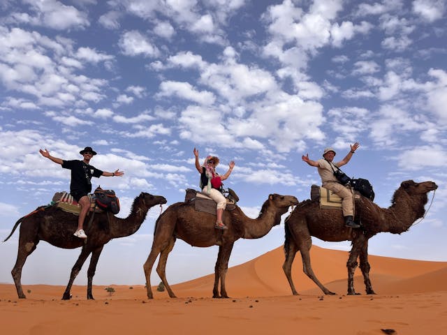 Tres turistas montando en camello en el desierto del Sahara bajo un cielo azul brillante.